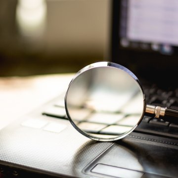 background check services cost price money magnifying glass on black laptop keyboard